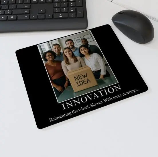Mouse mat with the text “INNOVATION – Reinventing the wheel. Slower. With more meetings” showing a group of office workers standing behind a cardboard box labelled “New Idea” — sarcastic corporate humor desk accessory.