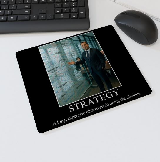 Mouse mat with the text “STRATEGY – A long, expensive plan to avoid doing the obvious” showing a businessman gesturing to a glass wall full of corporate buzzwords and diagrams — parody office desk accessory.