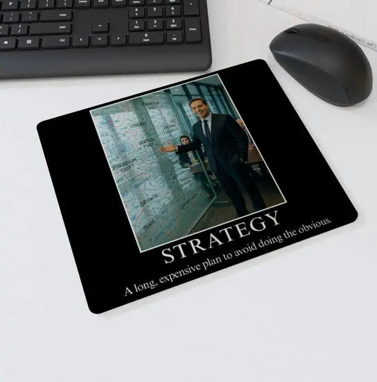 Mouse mat with the text “STRATEGY – A long, expensive plan to avoid doing the obvious” showing a businessman gesturing to a glass wall full of corporate buzzwords and diagrams — parody office desk accessory.