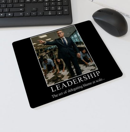 Mouse mat with the text “LEADERSHIP – The art of delegating blame at scale” showing a businessman pointing while employees crawl on the floor picking up papers — sarcastic office desk accessory.