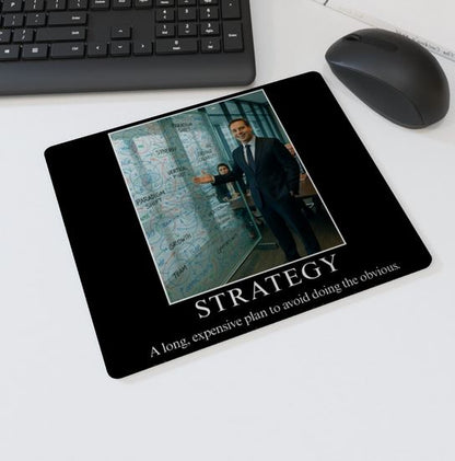 Mouse mat with the text “STRATEGY – A long, expensive plan to avoid doing the obvious” showing a businessman gesturing to a glass wall full of corporate buzzwords and diagrams — parody office desk accessory.